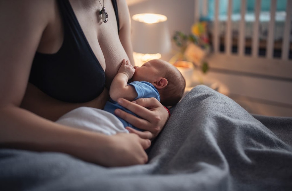 A parent breastfeeds a baby in a cozy bedroom setting.