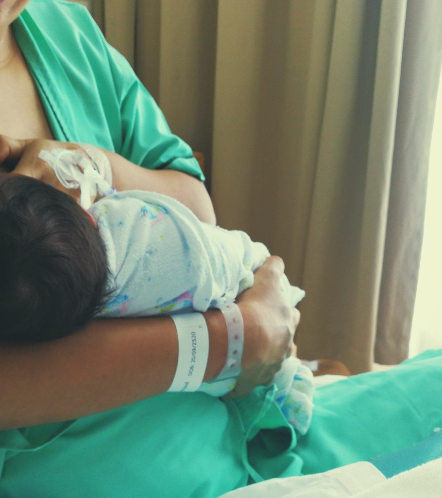 A parent holds a newborn while breastfeeding in a hospital setting.