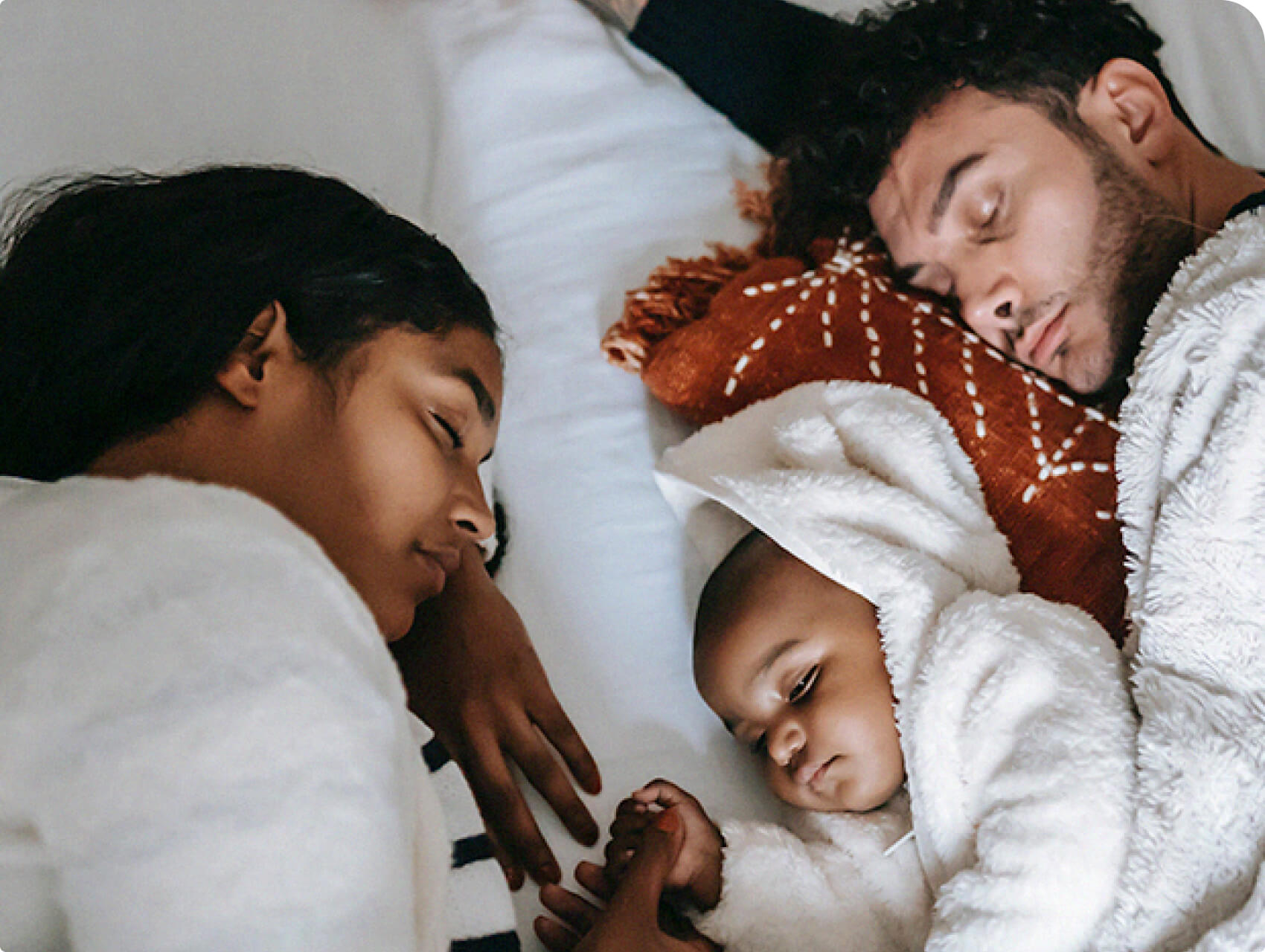 Parents resting in bed while holding closely holding their baby.