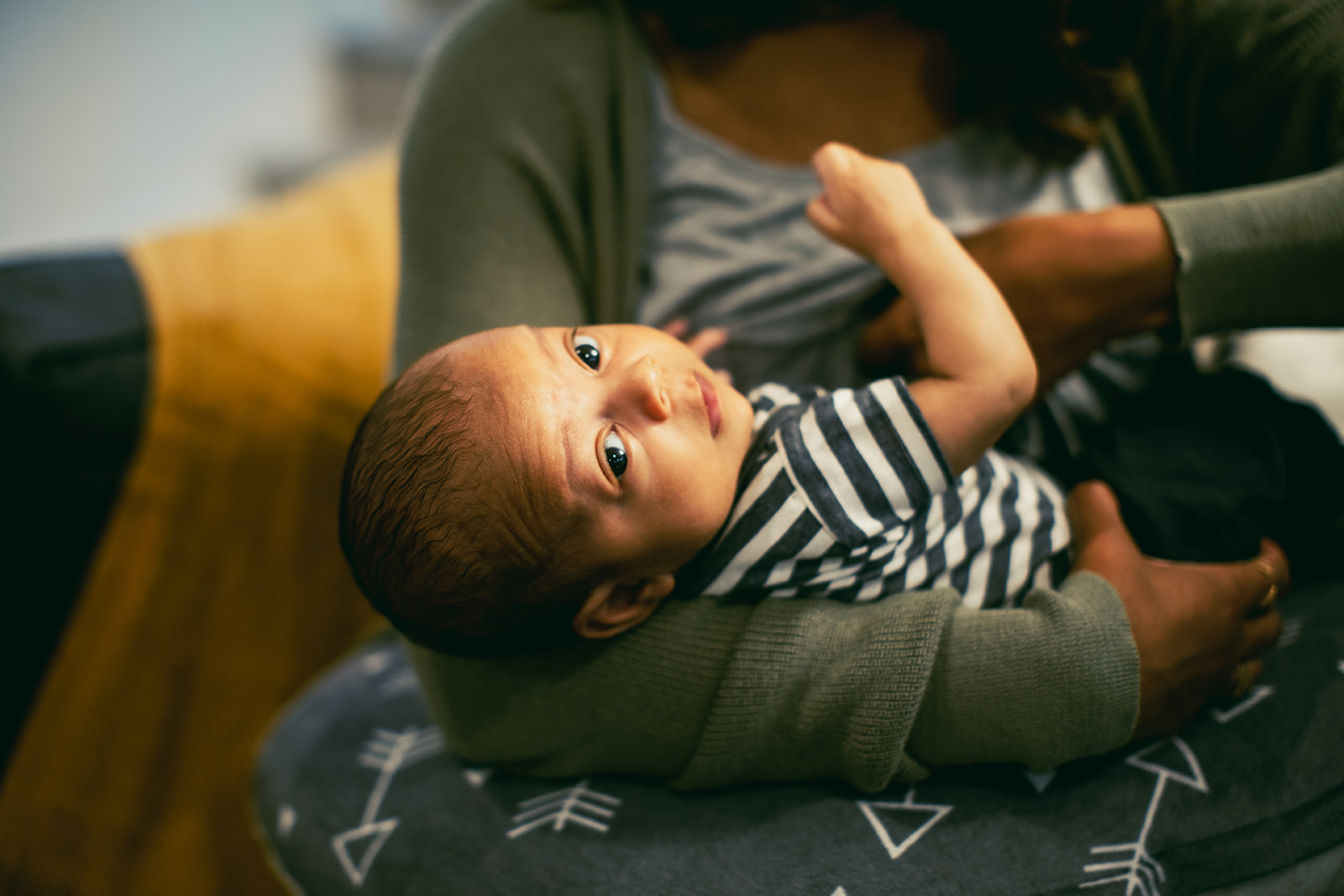 A baby in a striped shirt looks over its shoulder while being held by a caretaker