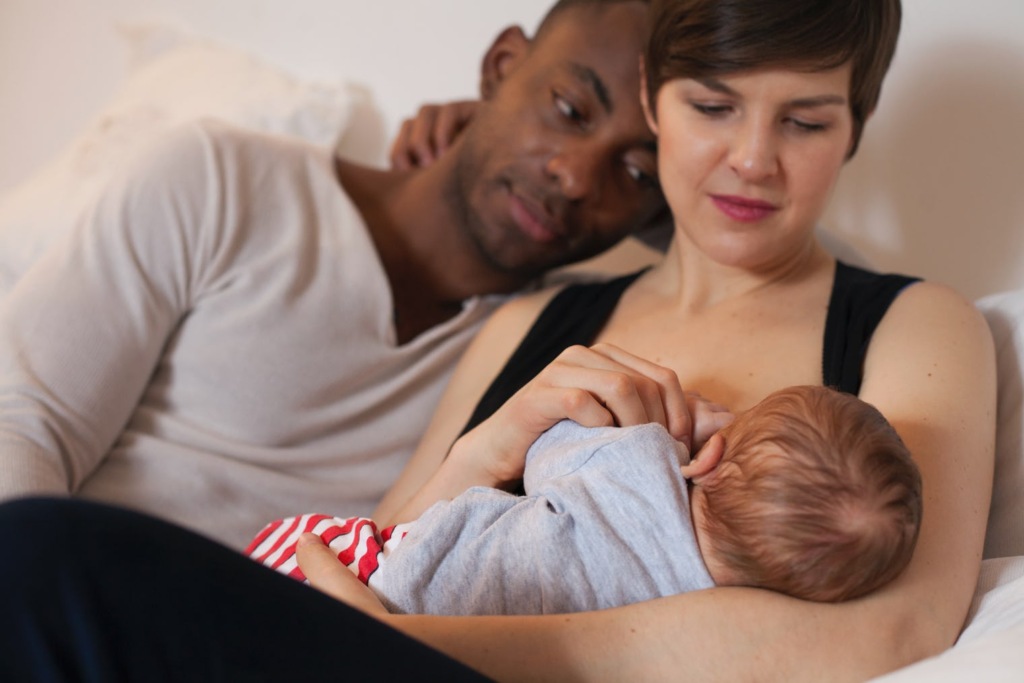 A couple lovingly watches their baby while breastfeeding.