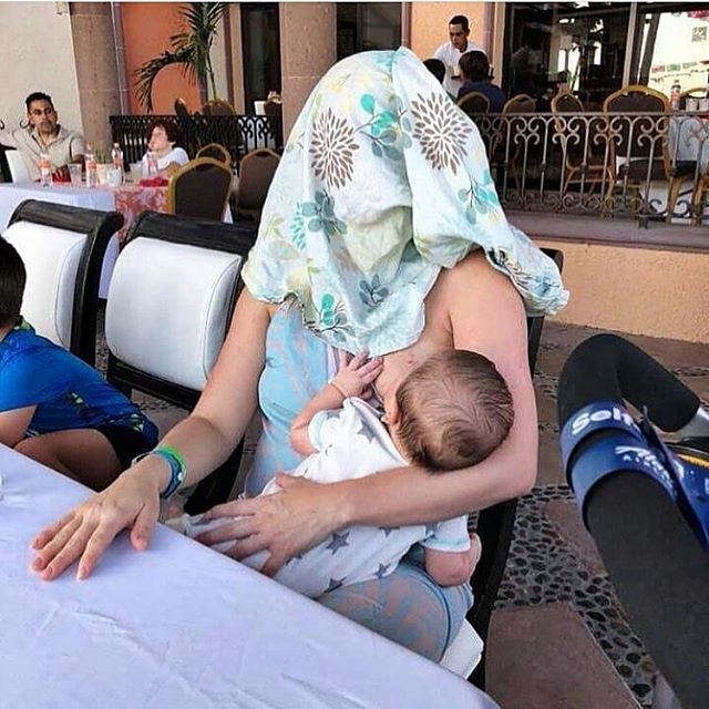 A parent breastfeeds in a public place with a blanket over their head