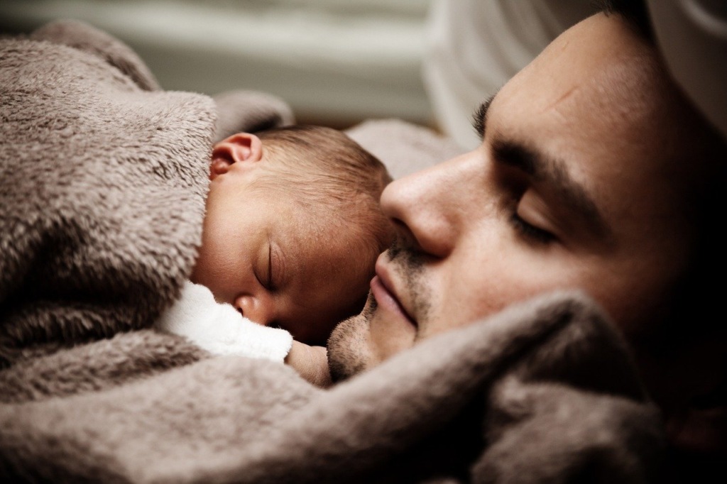 A parent and newborn baby sleeping peacefully together under a soft blanket.