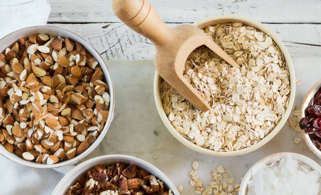 Two bowls are shown, one with dried oatmeal and the other with chopped almonds