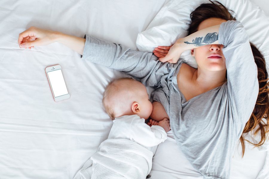 A parent lying down while breastfeeding their baby, with a smartphone resting nearby.