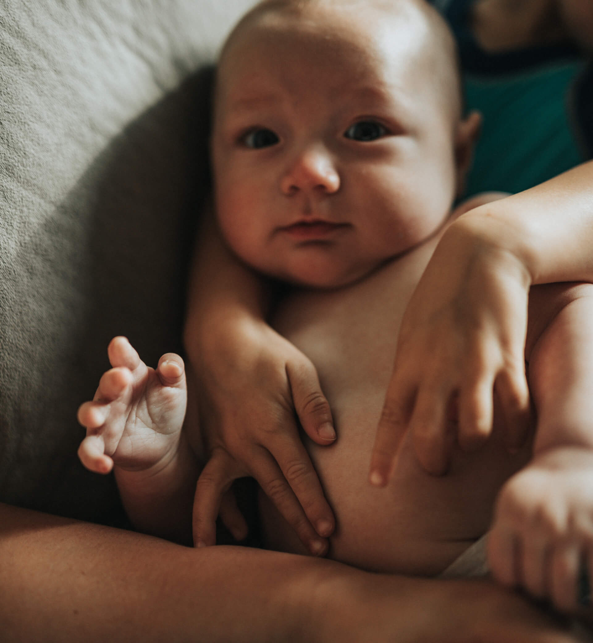 A baby smiling with two hands holding the baby close.