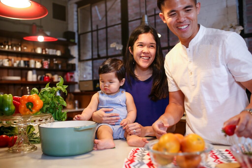 A parent smiles as they hold a baby seated on a kitchen counter