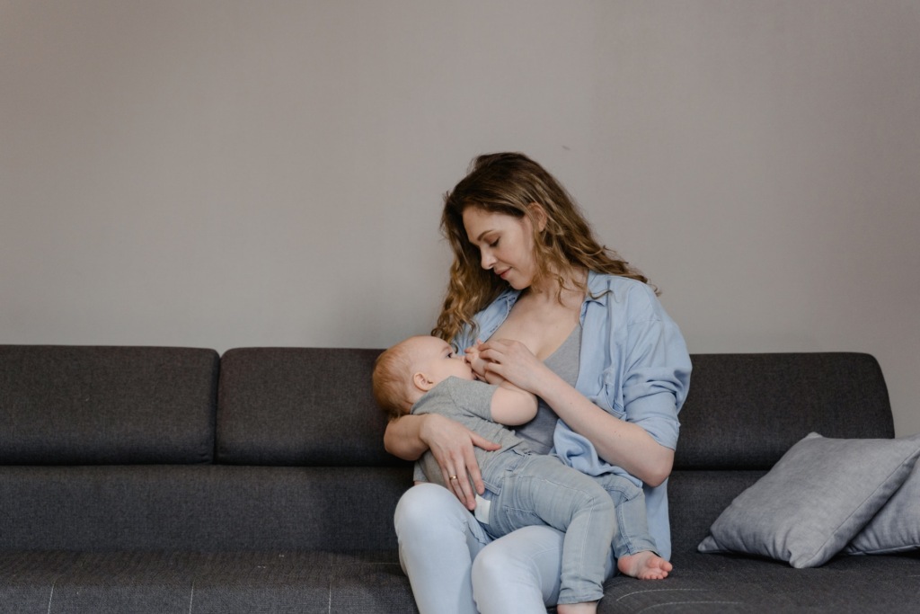 A parent breastfeeding their baby while sitting on a sofa.