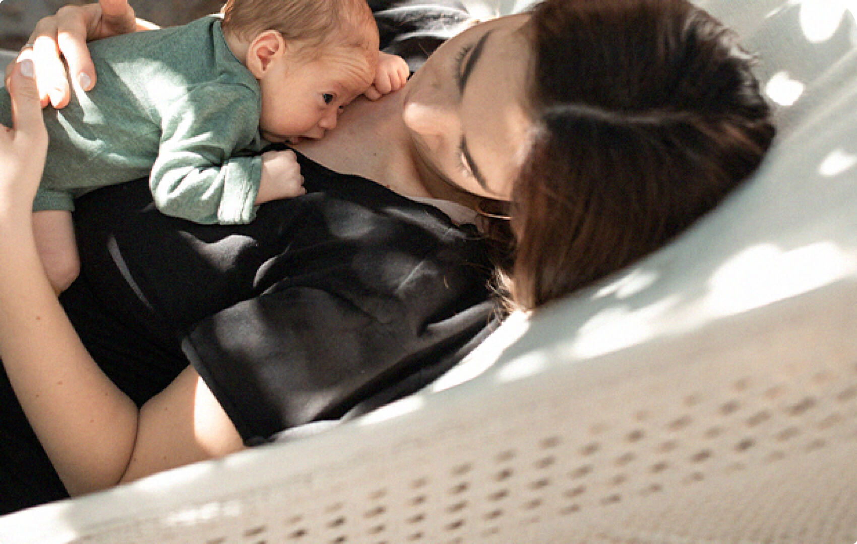 A parent and baby resting together in a hammock, with the baby gently resting on the parent's chest.