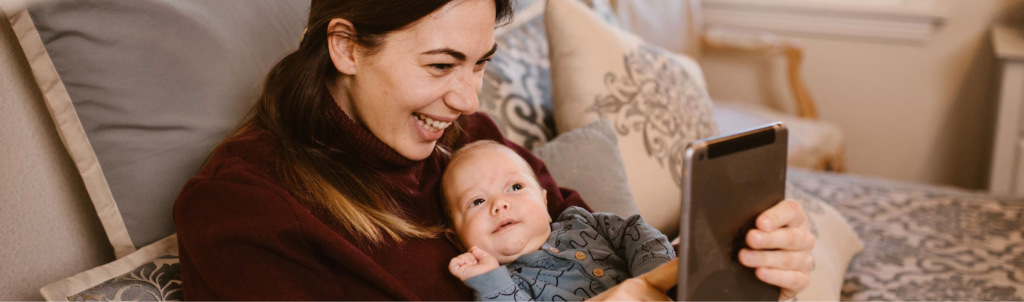 A parent and their baby sharing a joyful moment while looking at a tablet.