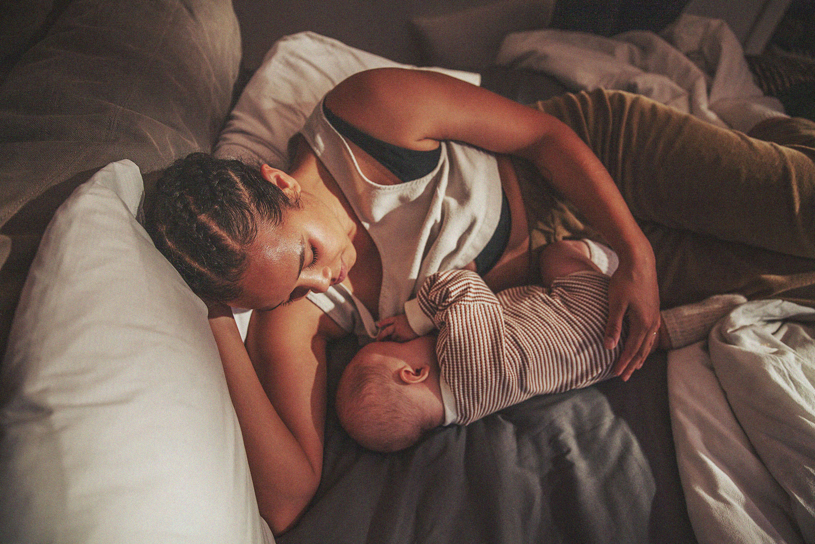 A parent breastfeeding a baby while lying on a bed.