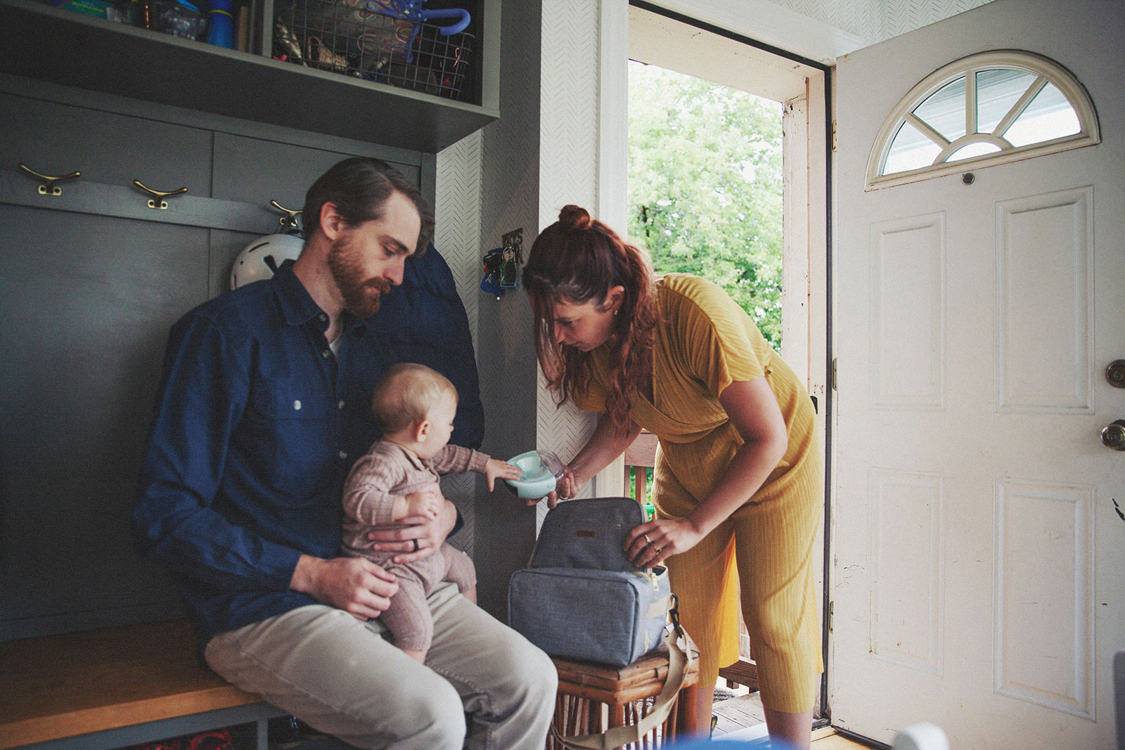 A family preparing for an outing, with one parent assisting the toddler and the other packing a bag.