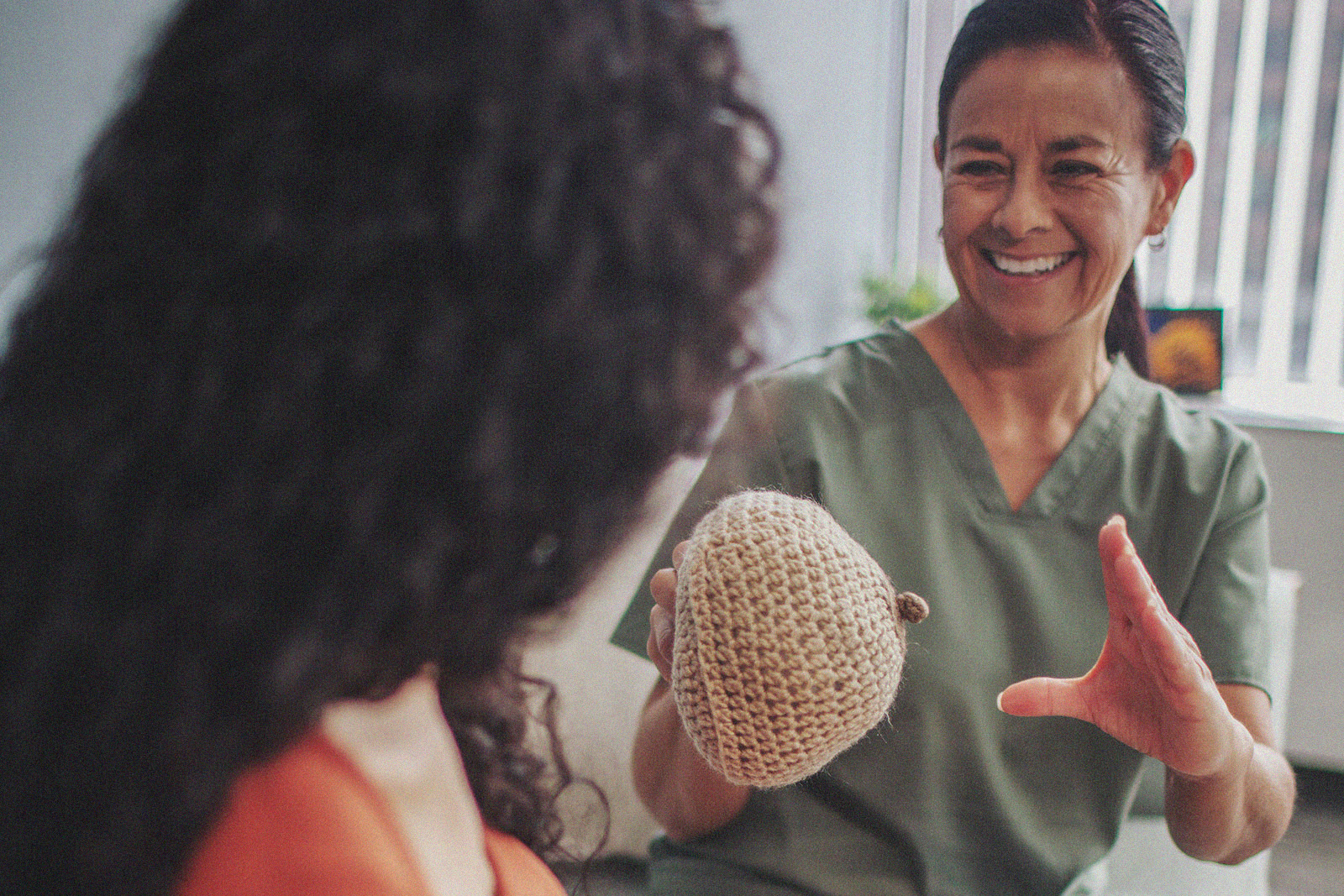 An International Board Certified Lactation Consultant demonstrates breastfeeding techniques to a parent using a knitted breast model.