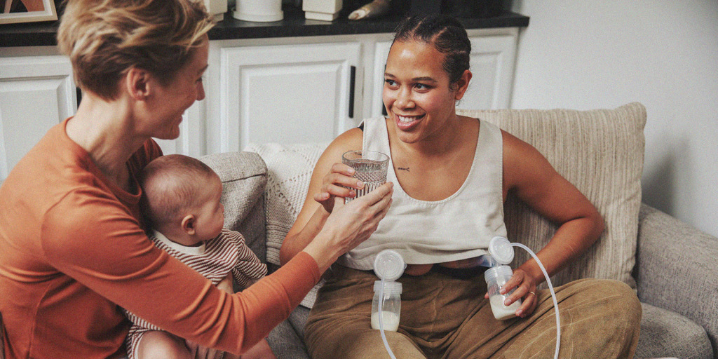 A parent pumping breast milk at home, receiving support and hydration from their partner.