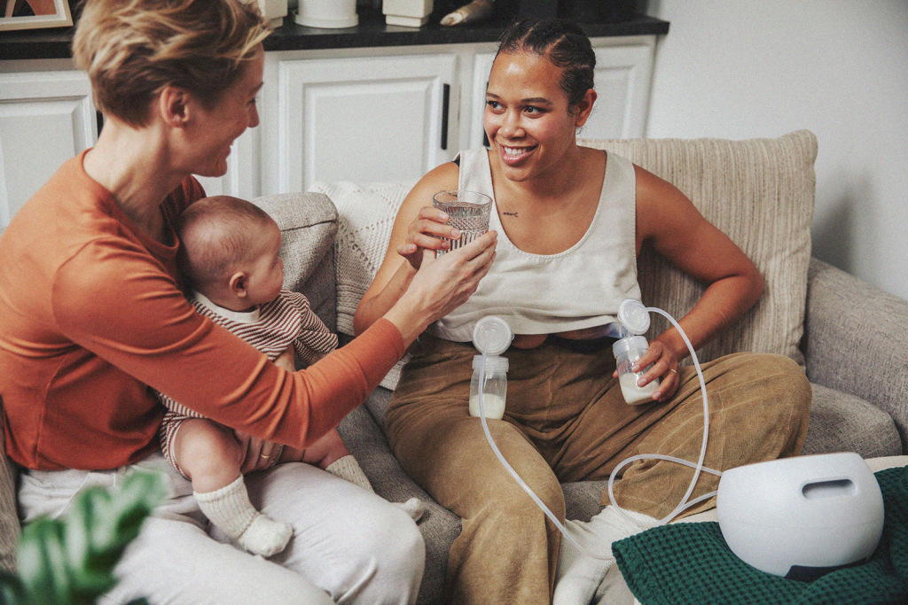 A parent pumping breast milk at home, receiving support and hydration from their partner.