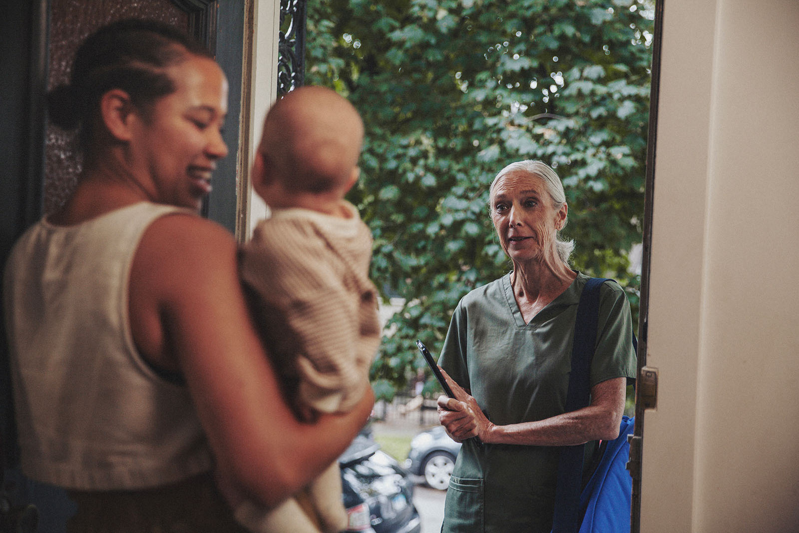 A parent joyfully greets an International Board Certified Lactation Consultant at the door while holding their baby.