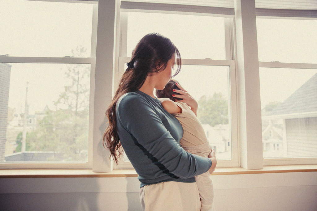 A parent cradles their child by the window, enjoying a quiet bonding moment.