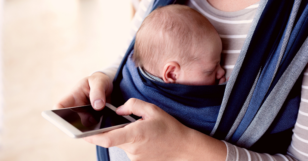 A person uses their mobile phone while their baby sleeps in a swaddle