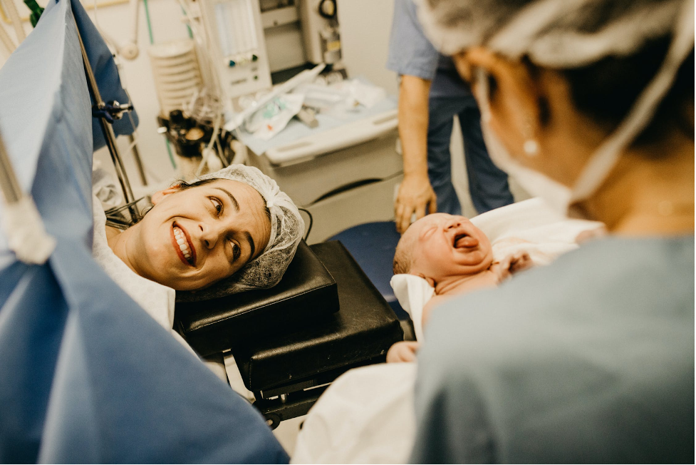 A parent who underwent a C-section smiles as they glance up at their recently delivered child.