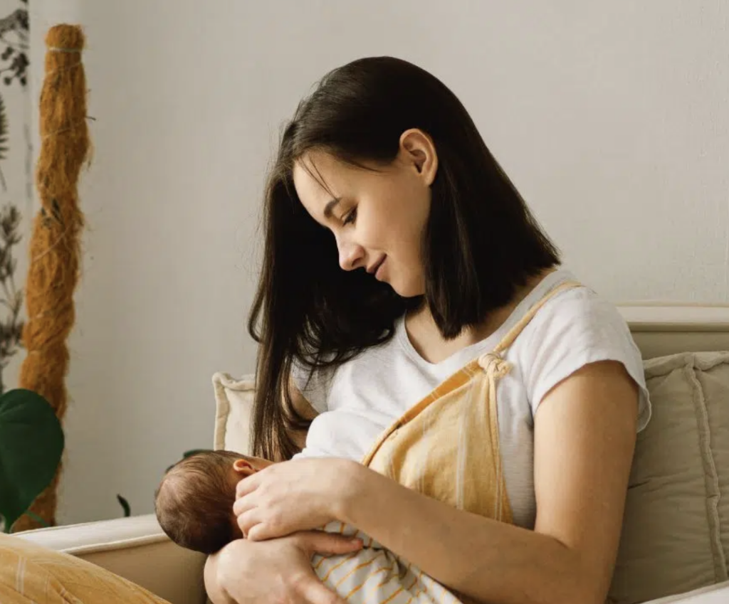 A parent breastfeeding their baby while sitting on a couch.