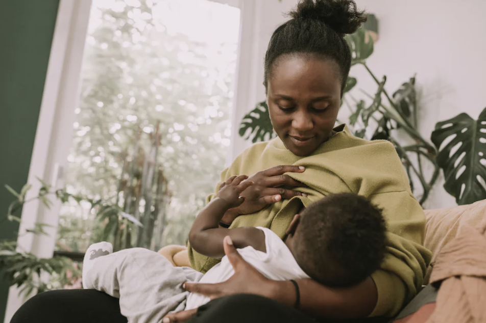 A parent breastfeeding their baby on a couch, with lush greenery in the background