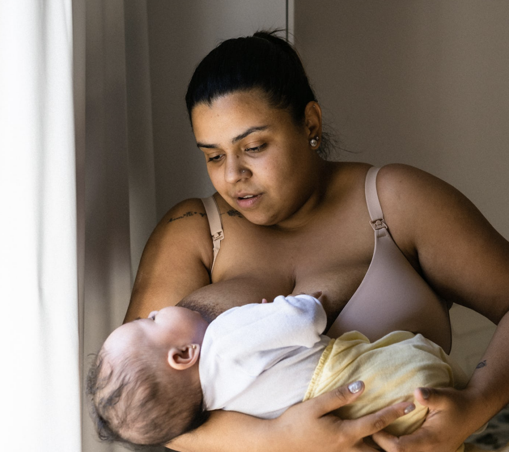A parent breastfeeding their infant in a bedroom.