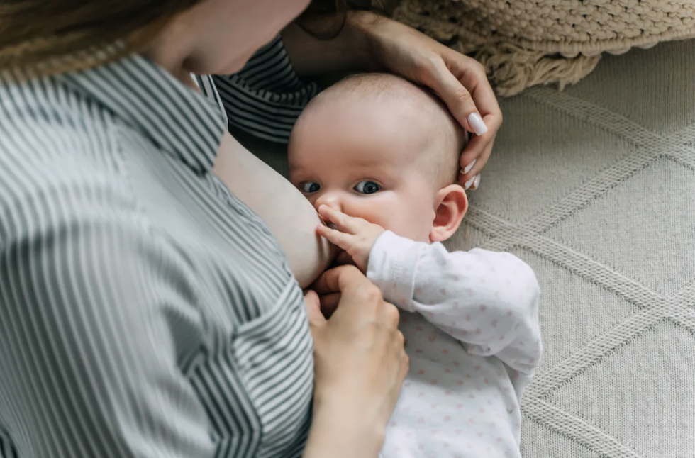 An infant breastfeeding while looking up at their parent.