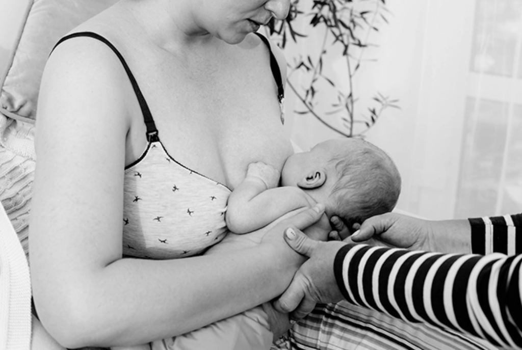 Two hands assisting a parent with positioning a newborn during breastfeeding.