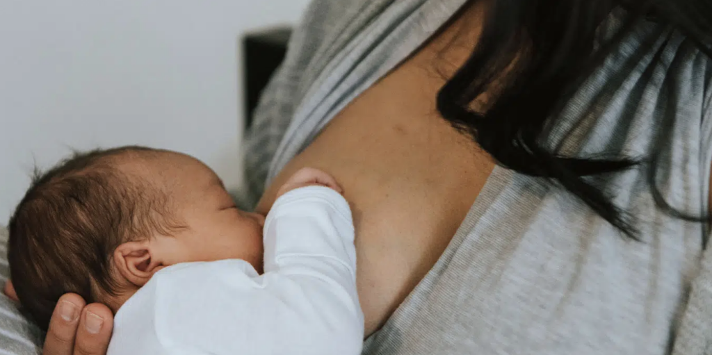 A close-up of a parent breastfeeding their newborn in a relaxed setting.
