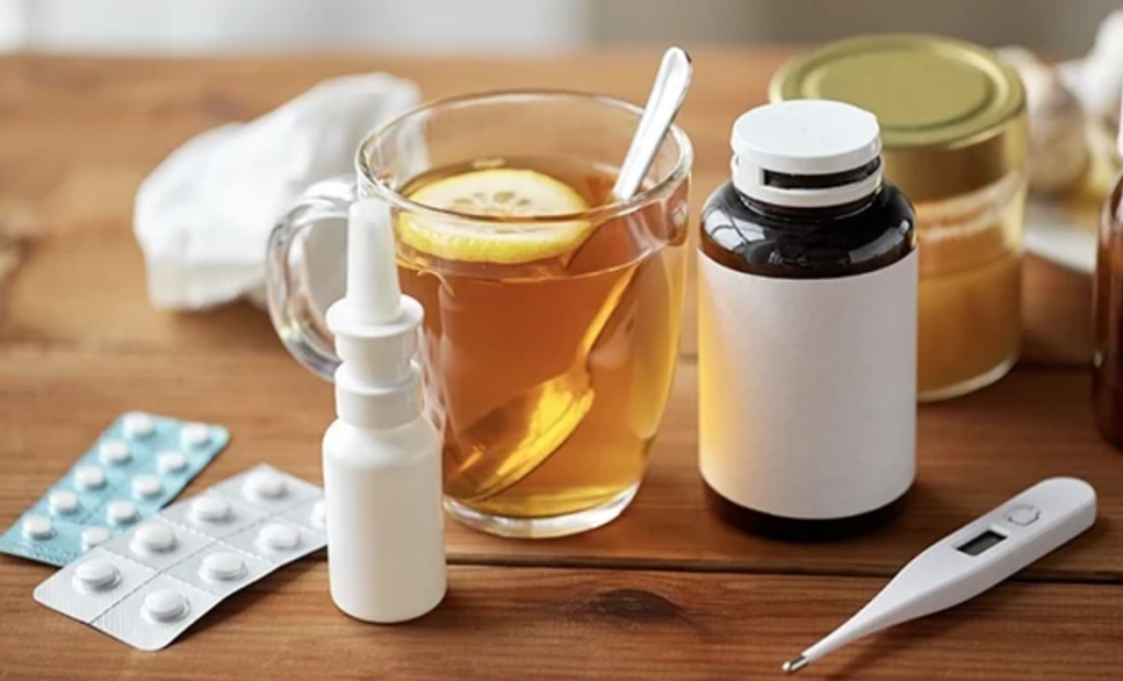 Thermometer, medications, and tea with lemon on a table, symbolizing self-care and wellness support.