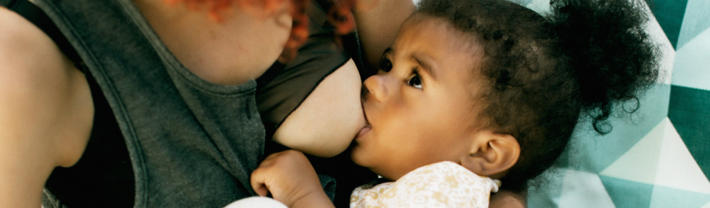 A close-up of a toddler breastfeeding and looking directly at their parent.