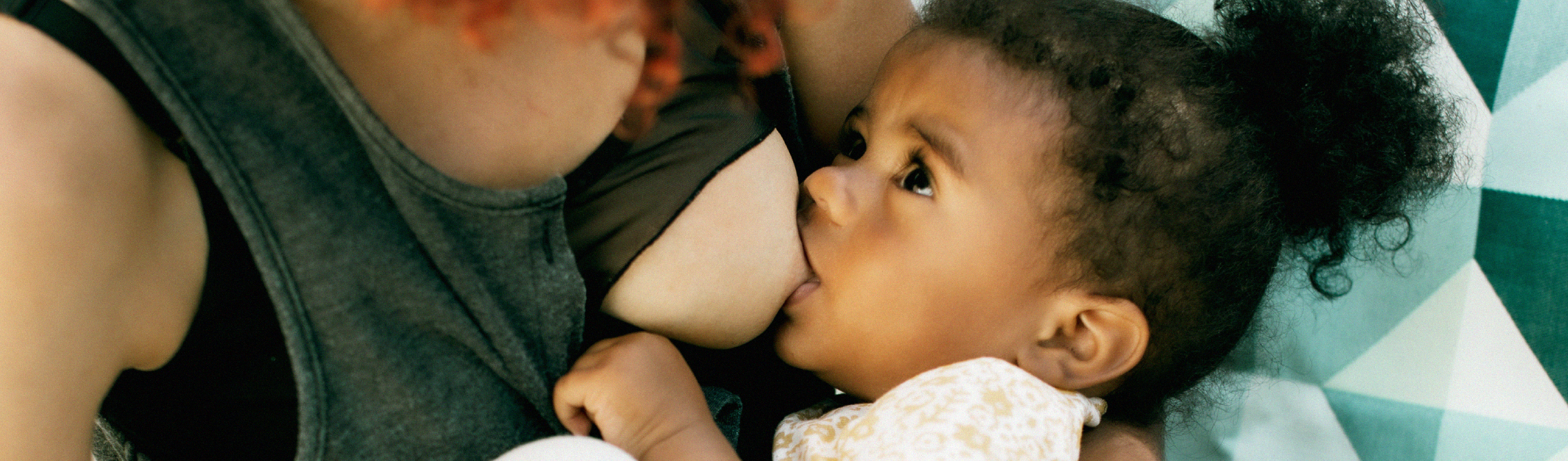 A close-up of a toddler breastfeeding and looking directly at their parent.