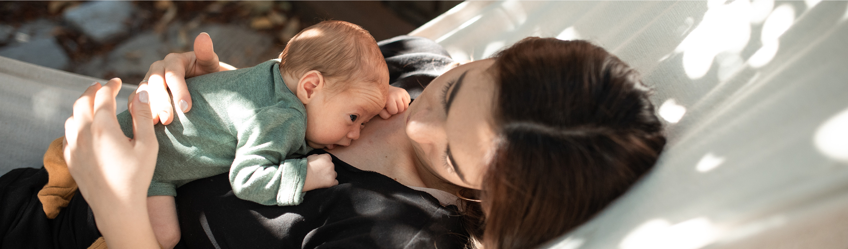 A parent and baby resting together in a hammock, with the baby gently resting on the parent's chest.